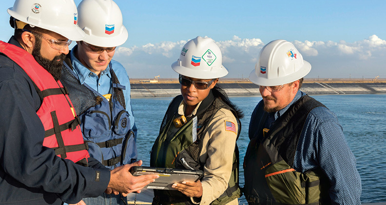 Four Yas Marina employees wearing hard hats at water's edge.